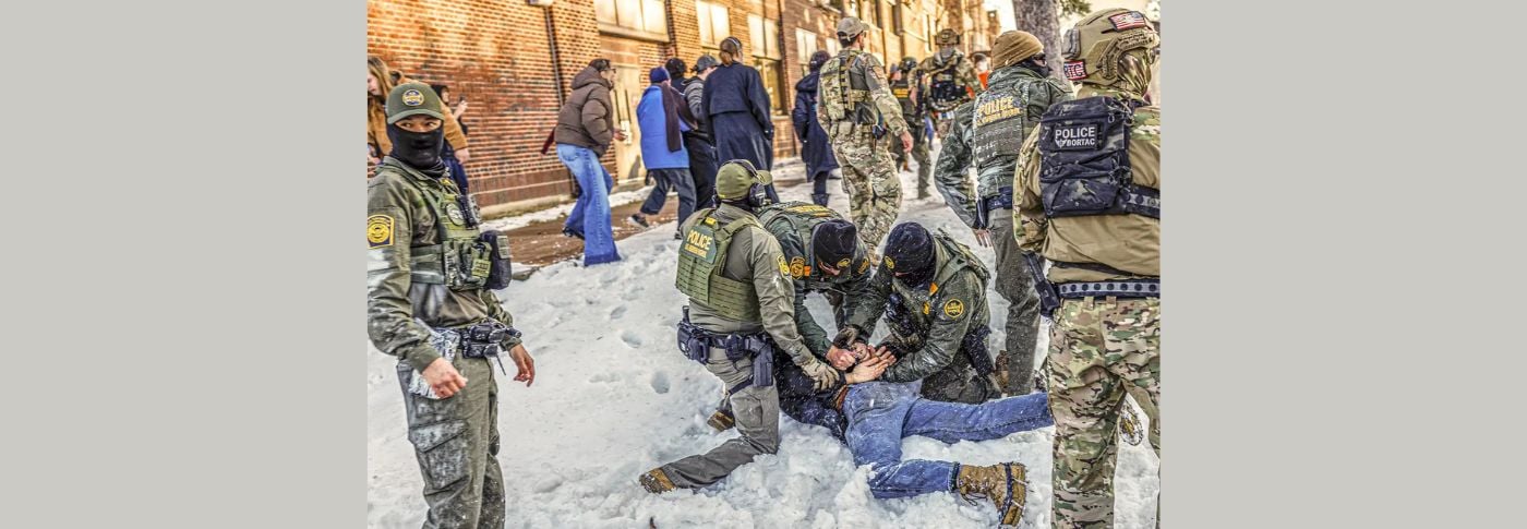 U.S. Border Patrol agents detain an individual on a snowy sidewalk near Roosevelt High School in Minneapolis during student dismissal, as immigration enforcement activity occurs near a school.